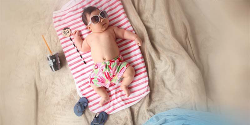 Baby-Krabbelgruppe geht in die Sommerpause; Foto eines Babys, das auf einem Laken am Strand in der Sonne liegt.