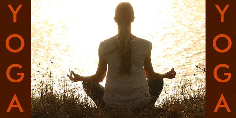 Yoga am Seeufer, Frau sitzt beim Yoga am Seeufer und im Hintergrund spiegelt sich die Sonne. UNklar, ob beim Sonnenaufgang oder beim Sonnenuntergang.